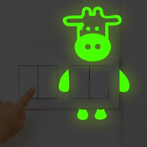 Glow-in-the-dark cartoon cow wall sticker showing luminous green effect near a power switch