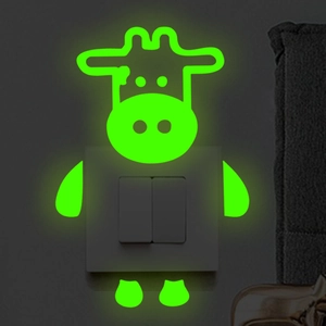 Luminous cartoon cow wall sticker glowing bright green on a light switch in the dark