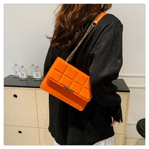 Detail of orange quilted crossbody bag with chain strap shown on model profile