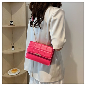 Close-up of pink quilted crossbody bag with gold chain strap on white blazer