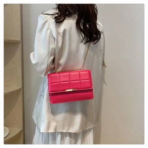 Detail of rose pink quilted square chain bag with golden clasp worn on white blazer