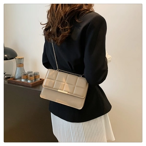Detail view of beige chain shoulder bag with lattice texture worn by a model