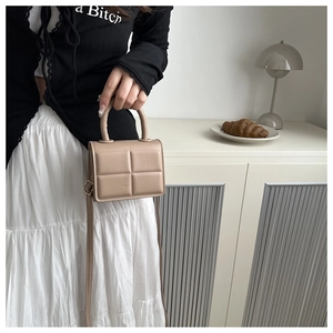 Mini beige textured PU handbag with round handle and shoulder strap shown in a lifestyle setting