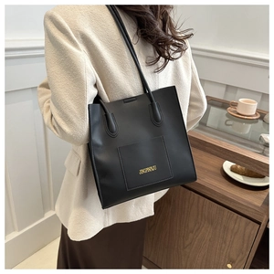 Détail du grand sac cabas noir en cuir PU avec logo doré et poche frontale sur un blazer beige