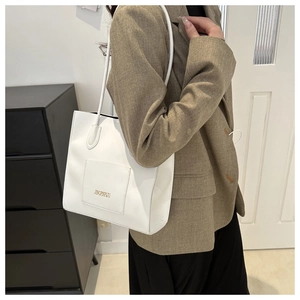 Détail du sac cabas en similicuir blanc avec lettrage doré porté sur un blazer marron