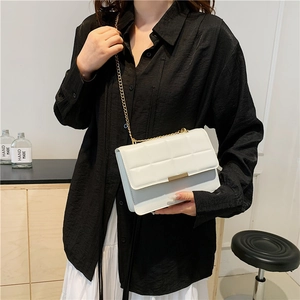 White quilted crossbody bag with gold chain strap and metallic lock shown on a model