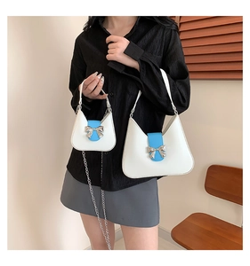 Detail view of stylish white leather saddle bag set with blue bow accent and chain strap