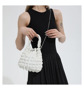 Detail of white bucket bag featuring bubble pleated texture and silver chain strap