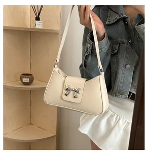 Detail showing creamy baguette bag with silver bow clasp on a minimalist shelf