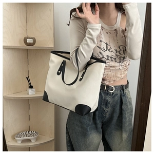 Detail of a large beige canvas tote bag with black leather trim and gold rivet reinforced handles