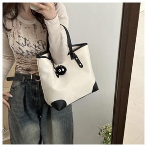 Detail of minimalist tote bag with black leather trim and cute plush monster charm