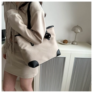 Detail of large canvas tote bag with black leather trim and plush ball accessory