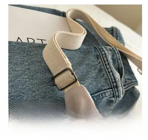 Detail view of adjustable metal buckle on beige canvas strap and blue denim handbag
