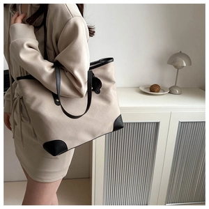 Detail of beige canvas tote bag with black leather trim and plush charm accessory