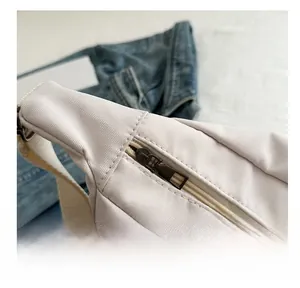 Detail of smooth bronze metal zipper on beige nylon crossbody bag with woven strap