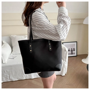 Detail of black high-capacity tote bag with gold rivet accents on striped shirt model