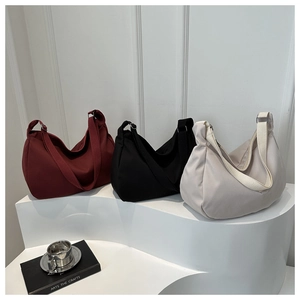 Three minimalist crescent shoulder bags in burgundy black and grey on white display steps