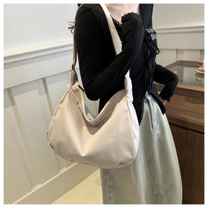Detail of a beige nylon crescent crossbody bag featuring a wide shoulder strap and zipper