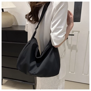 Minimalist black nylon hobo bag with adjustable wide strap shown on model's shoulder