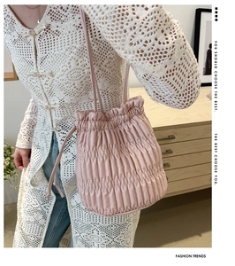 Detail view of light pink pleated bucket bag with drawstring closure and slim shoulder strap