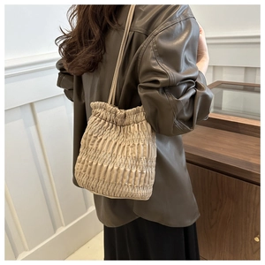 Detail showing beige pleated bucket bag with quilted texture on a stylish woman