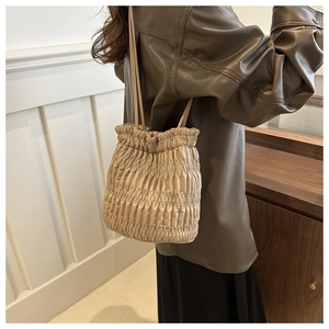 Detail of drawstring bucket bag featuring soft pleated quilting and cream faux leather finish