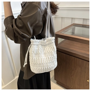 White pleated drawstring bucket bag styled with a leather shirt in a minimalist room