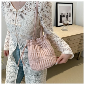 Detail shot of a pink pleated drawstring bucket bag styled with a white lace cardigan