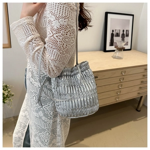 Metallic silver pleated bucket bag with drawstring and thin strap on person