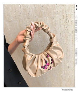 Detail of ruched beige underarm bag with purple butterfly print and pleated handle texture