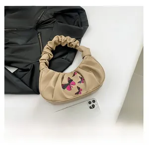 Detail of butterfly embroidery and pleated handle on the beige PU leather shoulder bag