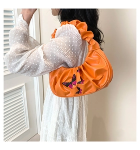 Detail of orange pleated underarm bag featuring colorful butterfly embroidery on soft PU leather