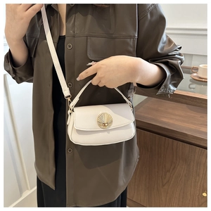 Detail view of a cream shoulder bag with shell clasp on a dark leather shirt