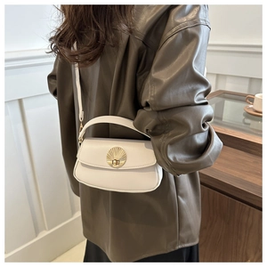 Detail of a beige underarm bag featuring a gold shell-shaped clasp worn by a model