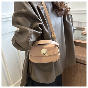 Close-up of golden shell buckle on leather crossbody bag worn by a model