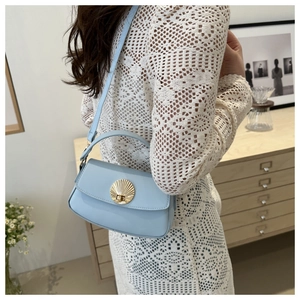 Detail of light blue crossbody bag with gold shell buckle worn by a model in soft lighting