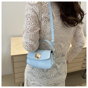 Detail of light blue crossbody bag with golden shell-shaped buckle and slim shoulder strap
