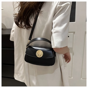 Detailed view of black leather crossbody bag with vintage gold shell buckle on model