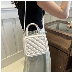 White quilted crossbody bag with top handle shown in a minimalist indoor setting