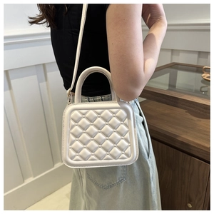 Detailed view of white quilted crossbody bag with top handle worn by a model