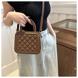 Close-up of brown quilted crossbody bag with gold hardware and top handle on a model