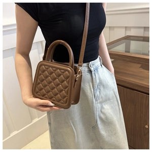 Close-up of brown quilted square crossbody bag with embossed texture and gold hardware