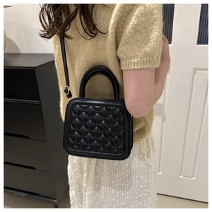 Detail of black quilted leather crossbody bag with top handle and gold hardware