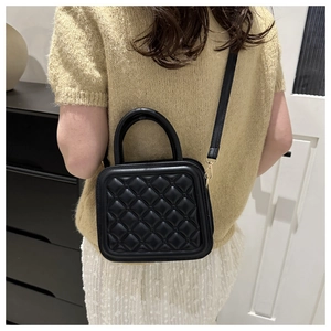 Detail of black quilted crossbody bag with top handle worn by a model in casual setting