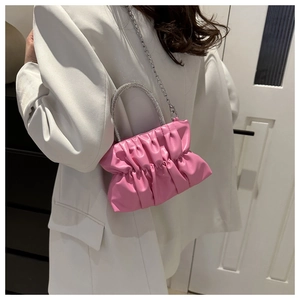 Roze geplooide emmertas met strass handvat en zilveren ketting op witte blazer gedragen