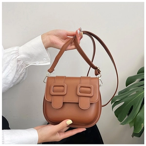 Detail of caramel faux leather saddle bag with dual decorative square buckles and gold hardware