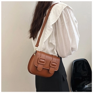 Detailed view of vintage brown matte leather saddle bag with double buckle straps on model