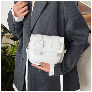 Close-up of white saddle bag with decorative straps on grey striped blazer