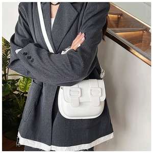 Close-up of a white vintage Cambridge saddle bag worn over a grey striped blazer