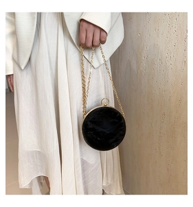 Detail of round black velvet evening bag with gold chain strap held by model